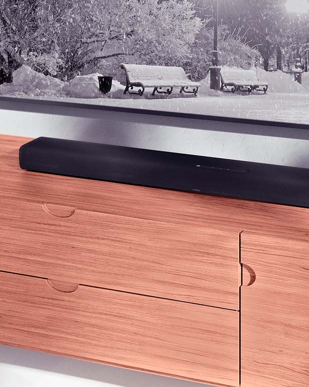 A Yamaha sound bar placed on wooden stand below a wall mounted television.