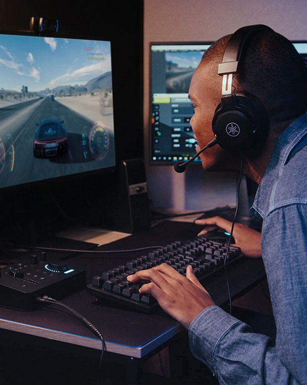 Person highly engaged and playing video games while using Yamaha gaming headphones and mixer.