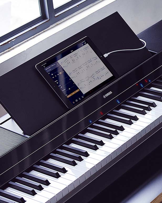 Closeup of a Yamaha digital piano connected to a tablet displaying music sheet.