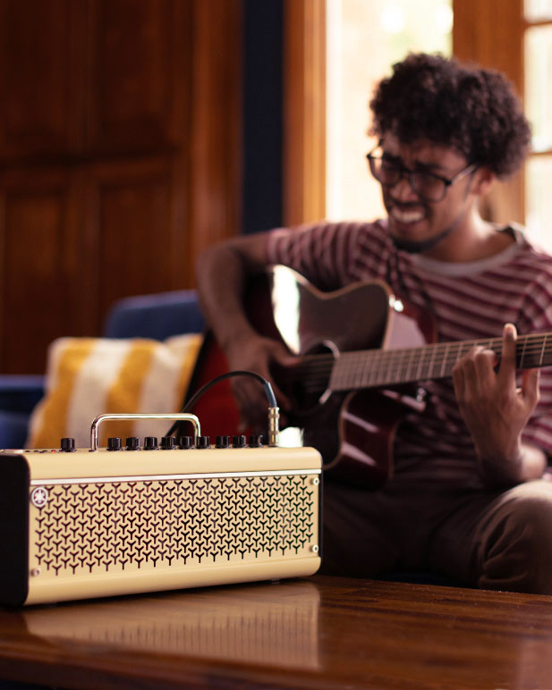 A Yamaha wireless guitar amp placed on a table with person playing the guitar in the background.