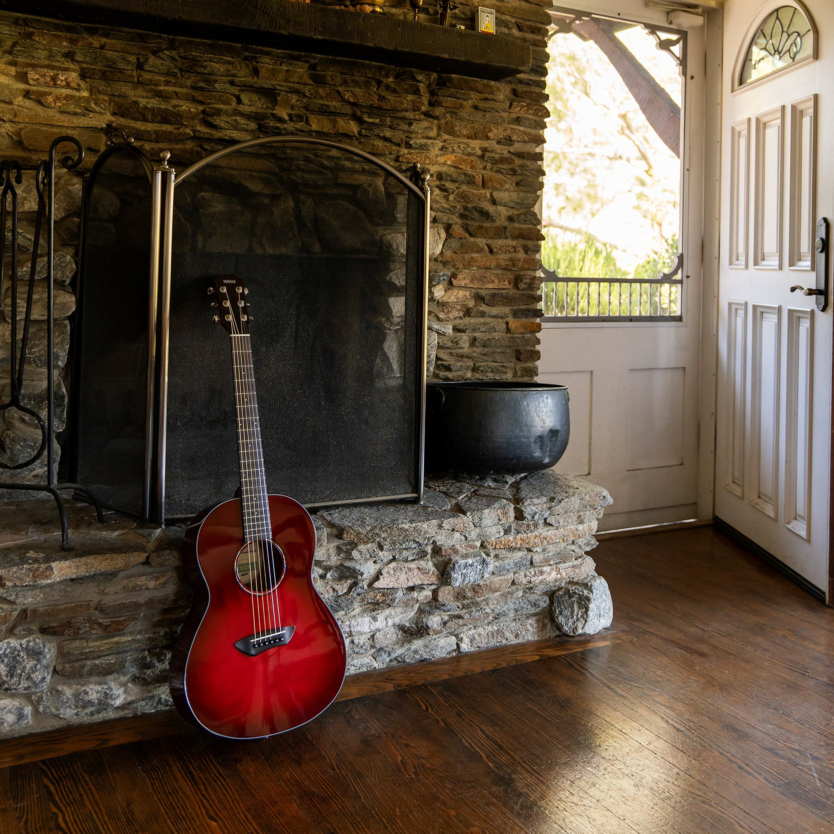 Guitar standing up leaning against a fireplace.